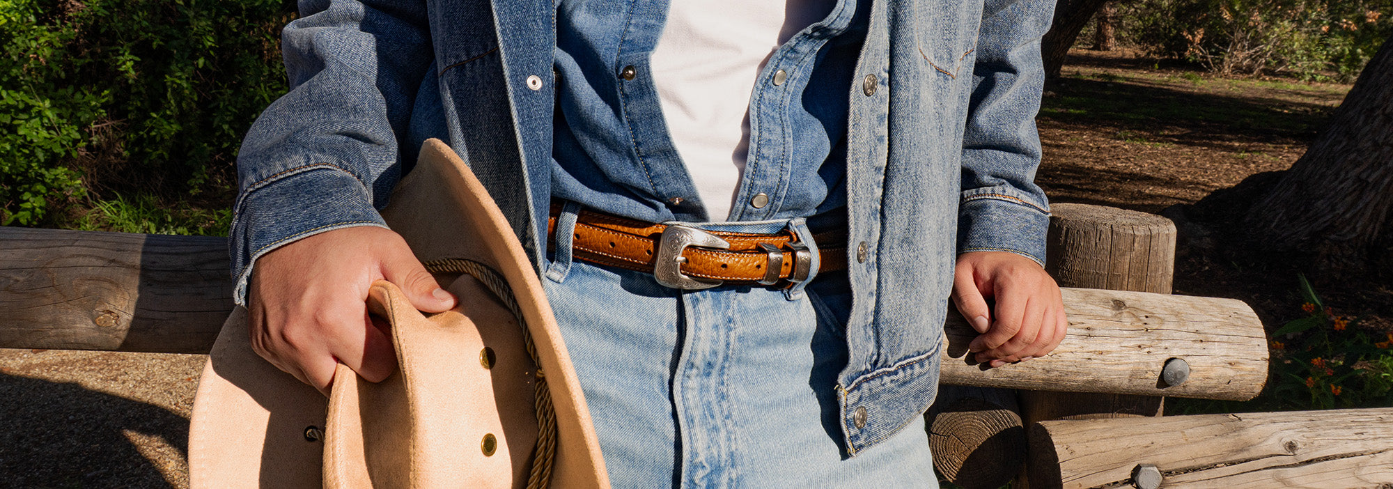 Person wearing a denim jacket and holding a hat outdoors