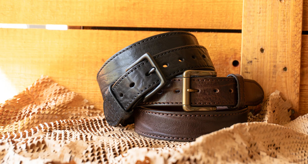 Two leather belts with brass buckles on a textured surface with wooden background