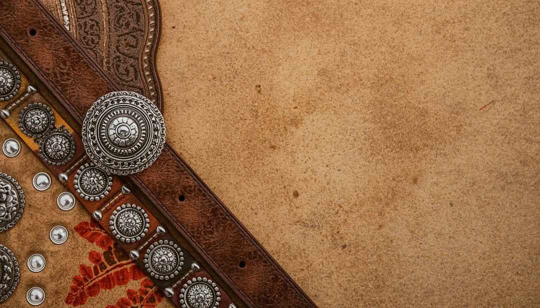 Close-up of a brown leather belt with decorative silver conchos on a textured brown background.